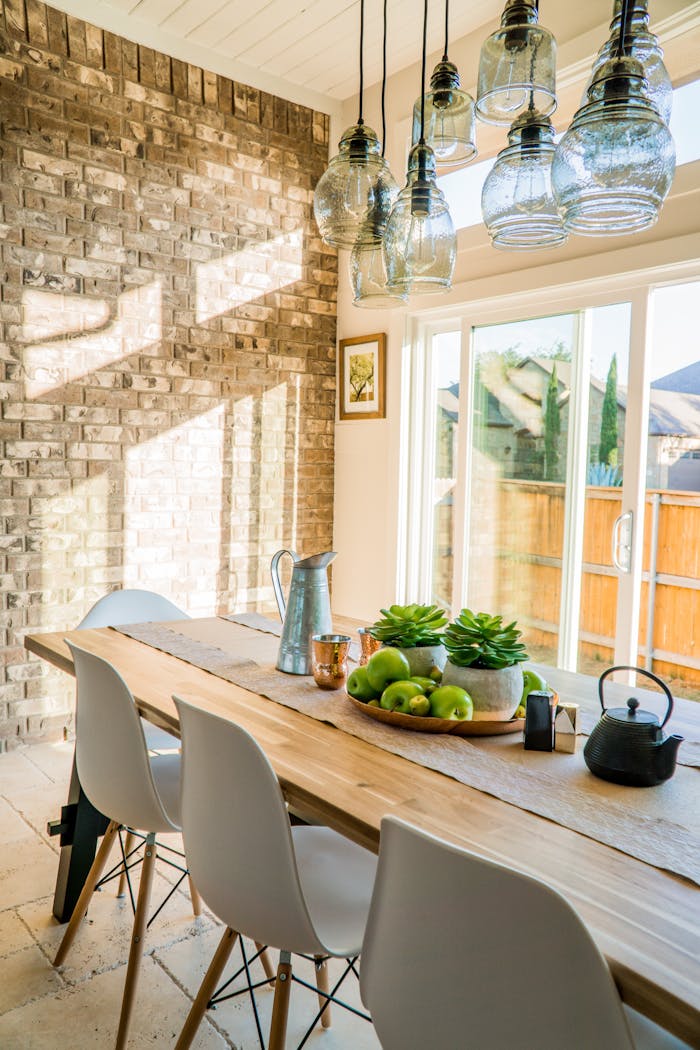 Contact Sunlit dining room with contemporary decor and a rustic brick wall, featuring stylish lighting and a wooden table.